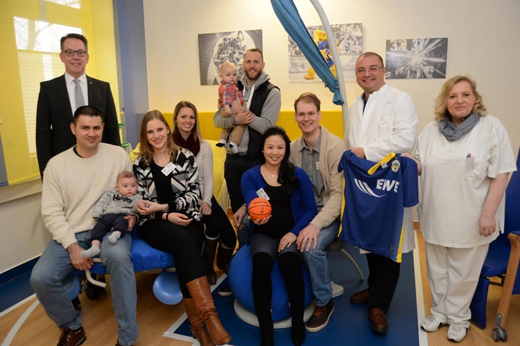 Dr. Dirk Tenzer, Mauricio Parra mit Sohn Alex und Ehefrau Rebecca, Maria und Spieler Vaughn Duggins mit Sohn Gianni, Angela und Basketballer Robin Smeulders, Prof. Dr. Eduard Malik und Hebamme Ines Schaeffer bei der Einweihung des EWE Baskets-Kreißsaal im Klinikum Oldenburg.