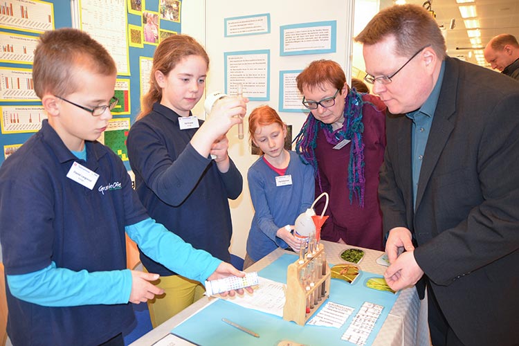 Daniel Langwost, Ida Krause und Charlotta Kruse erklären im Beisein ihrer Lehrerin Birgit Krah einem Besucher ihre Experimente.