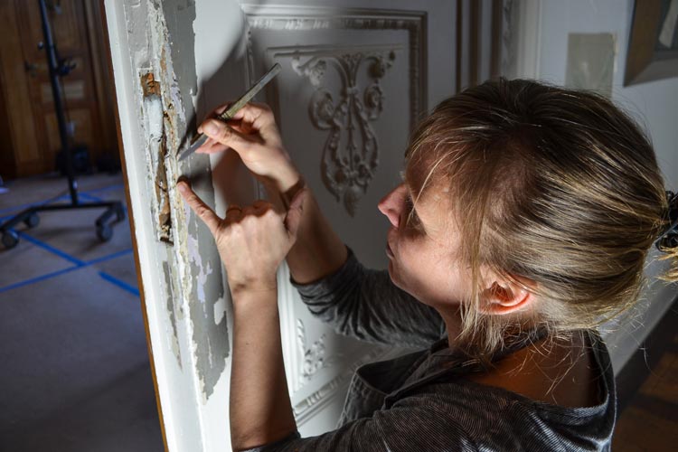 Britta Dierig löst mit einem Skalpell die einzelnen Farbschichten von der Holztür.