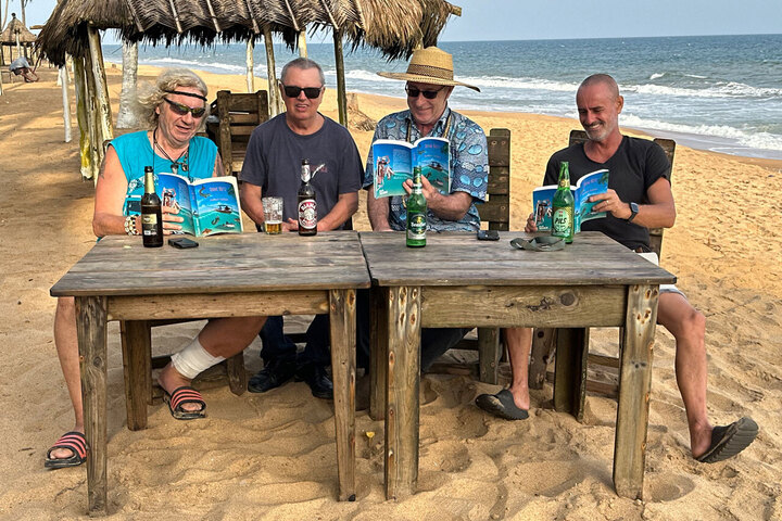 Strandlektüre mit Tiefgang: Herbert Hoddow (2. v. l.) teilt mit Freunden ein kühles Bier und sein Buch „Ohne Netz“ – Geschichten zwischen Abenteuer und Alltag in Nigeria.
