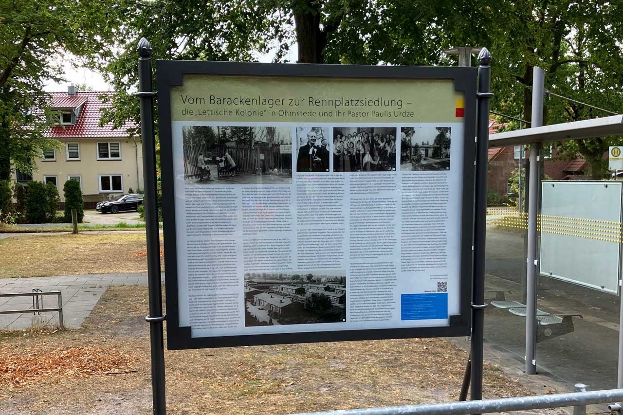 An die Geschichte der Rennplatzsiedlung, die Wurzeln in der Lettischen Kolonie und das Engagement des damaligen Pastors Paulis Urdze erinnert eine Infotafel am Kulturzentrum Rennplatz.