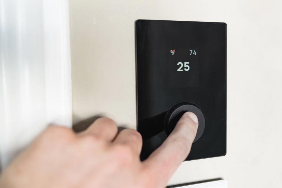 Hand dreht einen modernen smarten Thermostat an der Wand.